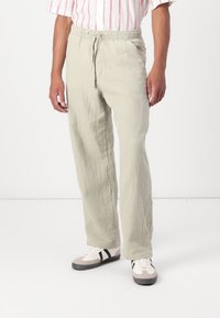 Light green linen pants with a relaxed fit, featuring an elastic waistband, drawstring closure, and textured fabric. Paired with casual sneakers.
