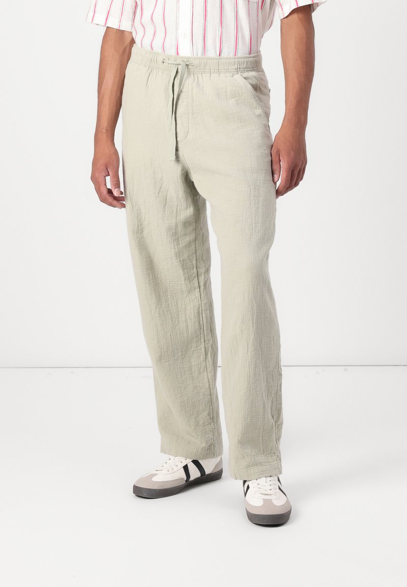 Light green linen pants with a relaxed fit, featuring an elastic waistband, drawstring closure, and textured fabric. Paired with casual sneakers.