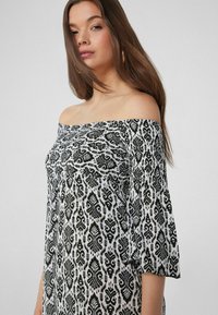 Vestido off-the-shoulder en blanco y negro. Presenta una tela estampada con diseños intrincados, mangas fluidas y un corte holgado.