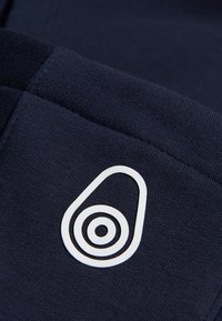 Tela azul marino con una textura suave que presenta un logotipo gráfico de aguacate blanco, caracterizado por una forma ovalada y círculos concéntricos.