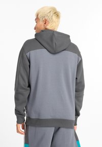 Sudadera con capucha gris y paneles en el hombro de un gris oscuro que contrasta. Presenta un corte holgado y una tela texturizada, adecuada para el uso casual.