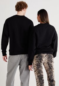 Sudaderas negras en dos figuras, una con pantalones grises y la otra con jeans de estampado de tigre, mostrando un ajuste relajado y una textura suave.