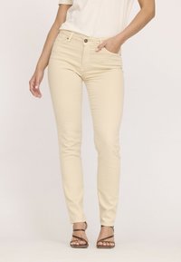 Jean beige ajusté en mélange de coton, avec une taille mi-haute, des poches avant et une fermeture à bouton classique.