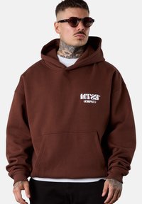 Hoddie marron avec une poche frontale, logo blanc sur la poitrine gauche, fabriqué en matériau doux, doté d'une capuche spacieuse et de poignets côtelés.