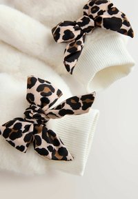 Witte fleece handschoenen met geribbelde manchetten, uitgerust met twee strikken van leeuwenprint in lichtbeige, zwart en bruine tinten.
