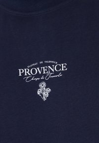 Tela azul marino con texto blanco "Plateau de Valensole Provence Champs de Tournesols" y una pequeña ilustración floral blanca debajo del texto.