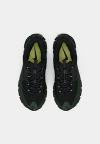 Baskets de sport noires et vert foncé avec une tige texturée, dotées d'une semelle rembourrée, de lacets ajustables et d'un logo Nike bien en vue sur la semelle intérieure.