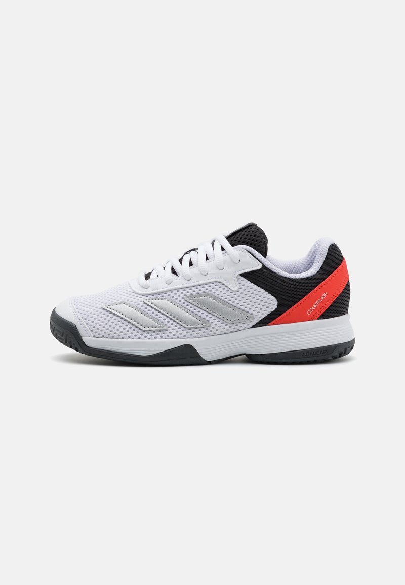 Zapatilla deportiva blanca con parte superior de malla, acentos negros y talón rojo. Presenta tres franjas plateadas y una suela de goma texturizada para mayor agarre.