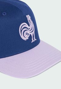 Gorra azul y lavanda con visera plana, con un emblema bordado en blanco de un gallo en el panel delantero. Tela texturizada.