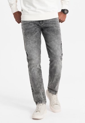 Harmaat farkut, jossa on haalistunut, kivipesutekstuuri. Slim fit -malli, yhdistettynä vaaleisiin tennareihin. Huomaamaton brändäys näkyvissä.