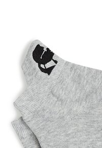 Calcetines grises con una textura suave que presentan un logo gráfico negro en el puño. El diseño es sencillo con una forma estándar.