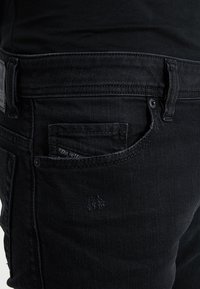 Svarta denimjeans med femficksdesign, som har sömnadsdetaljer, en liten logotyp på bakfickan och en slät, strukturerad yta.