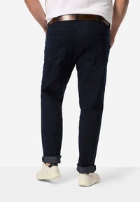 Tummansininen farkkuhousut, joissa on rento istuvuus, viisi taskua, käärityt lahkeet ja ruskea nahkavyö. Jalkineena valkoiset lenkkarit.