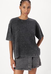 Svart acid-wash T-shirt med kort ärm och dekorativa pärldetaljer, i kombination med en matchande denimkjol. Strukturerad tyg, avslappnad passform.