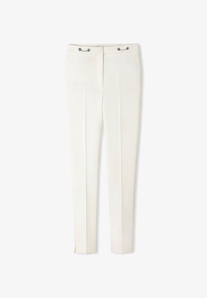 Pantalon blanc sur mesure avec plis sur le devant, poches latérales, détails en œillets métalliques à la taille et petites fentes latérales aux ourlets des chevilles.