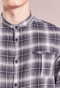 Szara i biała koszula w kratę z kołnierzykiem mandaryńskim, z guzikami na przodzie i kieszenią na lewej piersi z teksturowanej tkaniny.