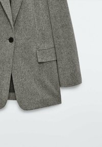 Szary �żakiet w wzór jodełki z czarnym guzikiem i kieszenią z klapką, zaprezentowany od połowy torsu do rękawa na białym tle.