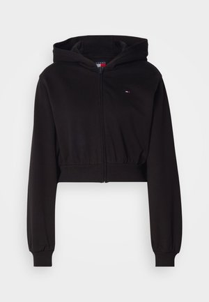 Zwarte cropped hoodie van zacht stof. Heeft een voorkant met rits, lange mouwen met elastische boorden en een logo op de borst.
