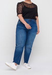 Haut en dentelle noire à manches courtes, associé à un jean taille haute bleu avec un ourlet effiloché. Porté avec des baskets blanches.