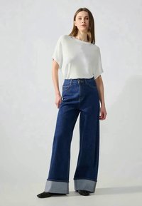 Bredde denimjeans i dyb blå med lyseblå ærmeafskærmninger, parret med en løs pasform hvid ribbet striktop.