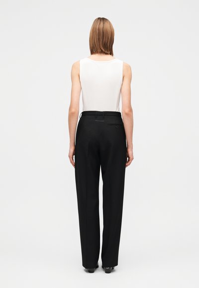 Haut blanc sans manches associé à un pantalon noir taille haute. Le pantalon présente une coupe près du corps avec une poche arrière unique et des passants pour ceinture.