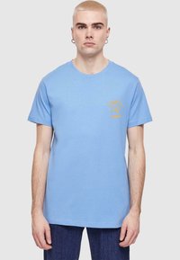 Light blue cotton t-shirt with a crew neck and short sleeves; features an orange graphic design on the left chest area.