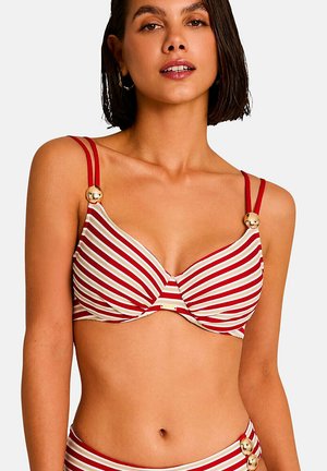 Femme portant un haut de bikini rayé rouge et blanc avec des bretelles doubles et des boutons dorés sur un fond uni.
