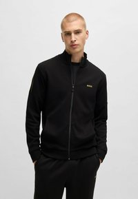 Zwarte zip-up jas van gladde stof, met een hoge kraag en het gouden "BOSS" logo op de linkerborst. Slim fit met geribbelde manchetten.