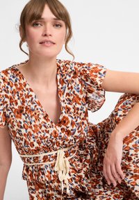 Blumenkleid mit tiefem V-Ausschnitt, kurzen Rüschärmeln und einem beigen Gürtel. Es hat einen mehrfarbigen Druck in Orange, Blau und Creme.