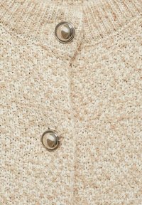 Beige neulottu neuletakki teksturoidulla kuviolla, jossa hopeinen nappikiinnitys kauluksessa. Pehmeä materiaali ja rento malli.