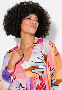 Robe à motifs colorés avec décolleté en V, manches longues et taille froncée. Fabriquée en tissu léger avec un mélange de designs abstraits.