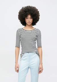 T-shirt ajusté rayé noir et blanc avec des manches trois-quarts. Associé à un pantalon bleu clair avec poches latérales et une texture lisse.