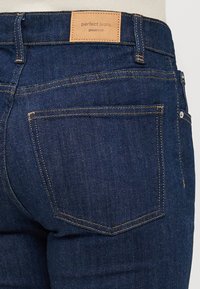 Dark blue denim jeans with a leather tag labeled "perfect jeans" at the waistband. Features two back pockets with visible stitching details.
