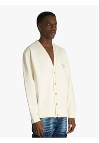 Cardigan crema con scollo a V e chiusura con bottoni, presenta cuciture arancioni a contrasto e un piccolo logo sul petto sinistro.