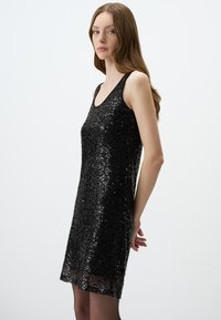 Robe noire sans manches recouverte de sequins, avec un décolleté rond et une coupe droite, dotée d'un ourlet transparent et d'une texture lisse.