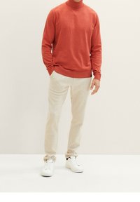 Rode coltrui, beige op maat gemaakte broek en witte sneakers. Zachte stof, getailleerd ontwerp, met opgerolde mouwen en minimale details.