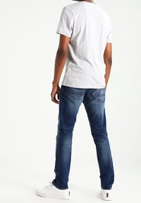 Grå kortärmad T-shirt, blå slim-fit jeans, vita sneakers. T-shirten har en rund hals; jeansen har bakfickor.