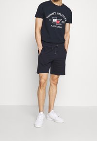 Navy cotton t-shirt with white and red logo, paired with matching navy shorts featuring an elastic waistband and drawstring. White sneakers.