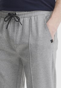 Grå sweatpants lavet af blødt materiale har en elastisk talje med snor, sidelommer og et lille logo-patch på hoften.