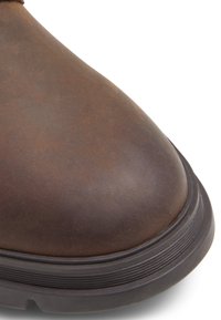 Bota de cuero marrón con punta redondeada, superficie texturizada y suela de goma negra con acentos estriados.