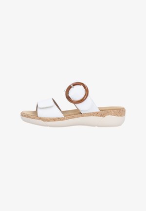 Sandales blanches à enfiler avec deux lanières, dont une avec une grande boucle circulaire marron. Semelle beige texturée avec un motif tissé. Design décontracté.