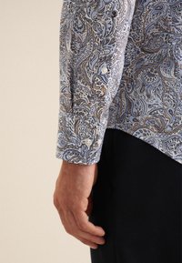 Niebieska koszula w wzór paisley z guzikami przy mankietach oraz dopasowanym krojem, wykonana z teksturowanej tkaniny, zdobiona szczegółowymi wzorami w odcieniach beżu i granatu.