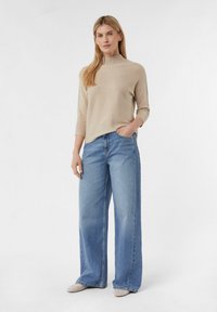Beige geribbelde gebreide trui met een hoge hals, gecombineerd met lichte denim jeans met brede pijpen en beige instappers.