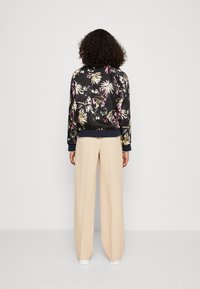 Bloemen bomberjack met zwarte basis, voorzien van veelkleurige tropische patronen. Gecombineerd met lichtbeige, wijde broek en witte sneakers.