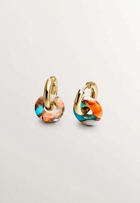 Pendientes de aro dorados adornados con cuentas cirulares con patrones de coral, turquesa y blanco; el acabado suave y vidrioso contrasta con el metal.