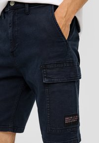 Granatowe szorty cargo wykonane z mocnego materiału, z bocznymi kieszeniami, przednią kieszenią z srebrnym guzikiem oraz naszywką z logo na nodze.