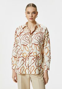 Long-sleeve shirt in light cream with abstract red and orange floral patterns, buttoned front, and a classic collar. Soft, textured fabric.