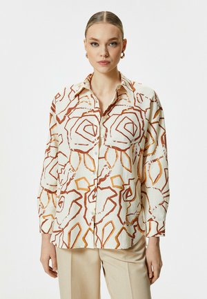 Langärmliges Hemd in hellem Creme mit abstrakten roten und orangefarbenen Blumenmustern, geknöpfter Front und klassischem Kragen. Weicher, strukturierter Stoff.