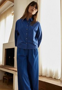 Chemise bleu ample à boutons avec des manches longues, associée à un pantalon bleu ample. Tissu doux et design simple avec un fini subtil.