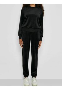 Tuta in velour nera caratterizzata da una maglia a vestibilità rilassata con scollo rotondo e polsini elasticizzati, abbinata a pantaloni coordinati con polsini elasticizzati.